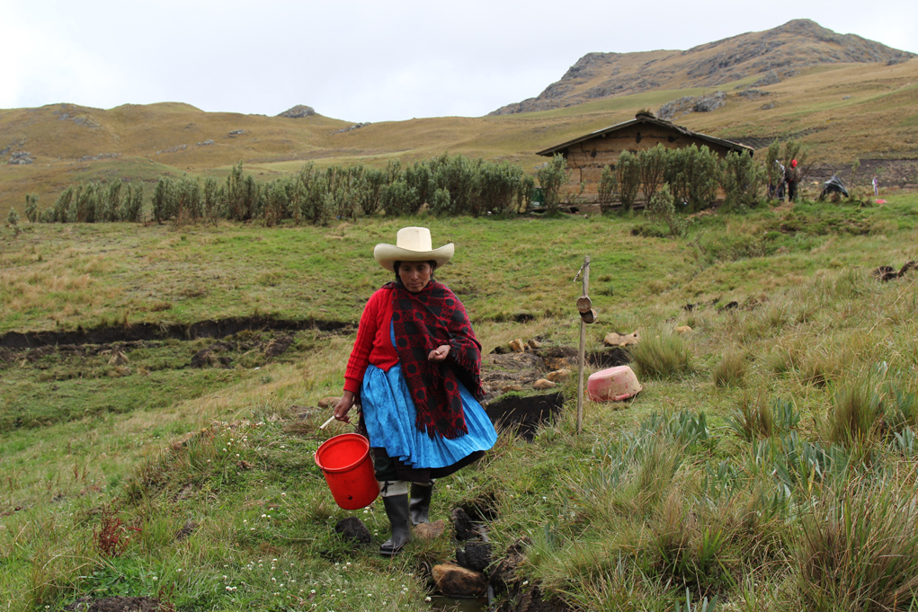Acuña working the land, her house stands in the background. 