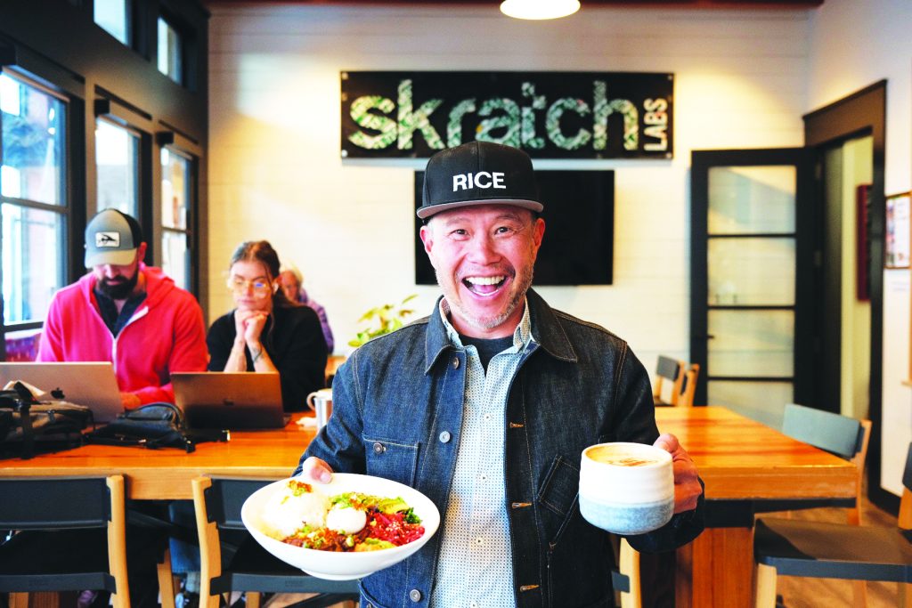 Smiling Allen Lim holds a plate of food and a drink at Skratch Labs in downtown Boulder