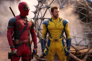 The Marvel Comics characters Deadpool and Wolverine, in their respective red and yellow superhero costumes, stand in the foreground against a spiky metal orb.