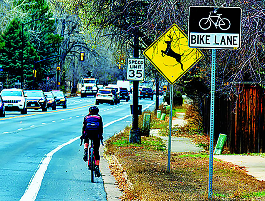 man biking on roadway next to cars and deer crossing and 35 mph speed limit sign with trees