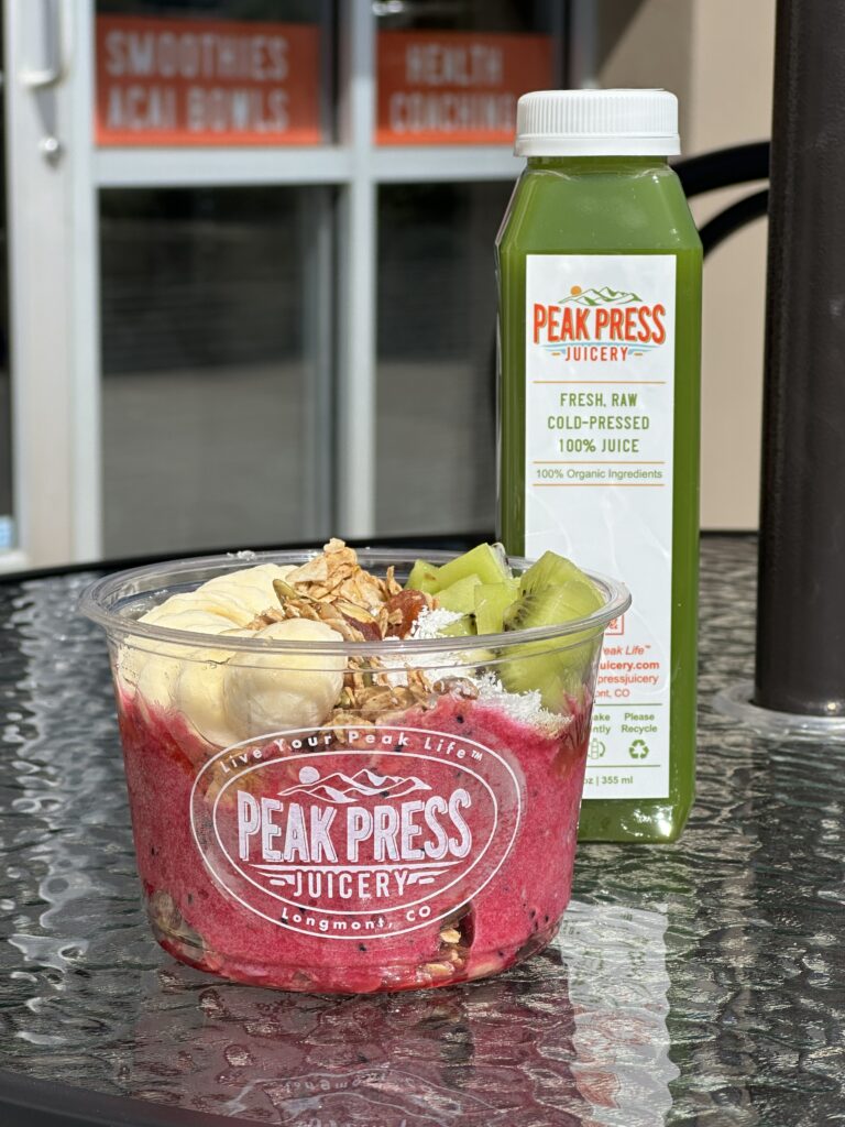 fruit and blended bowl and green juice from Peak Press Juicery in Longmont on glass table in front of white window