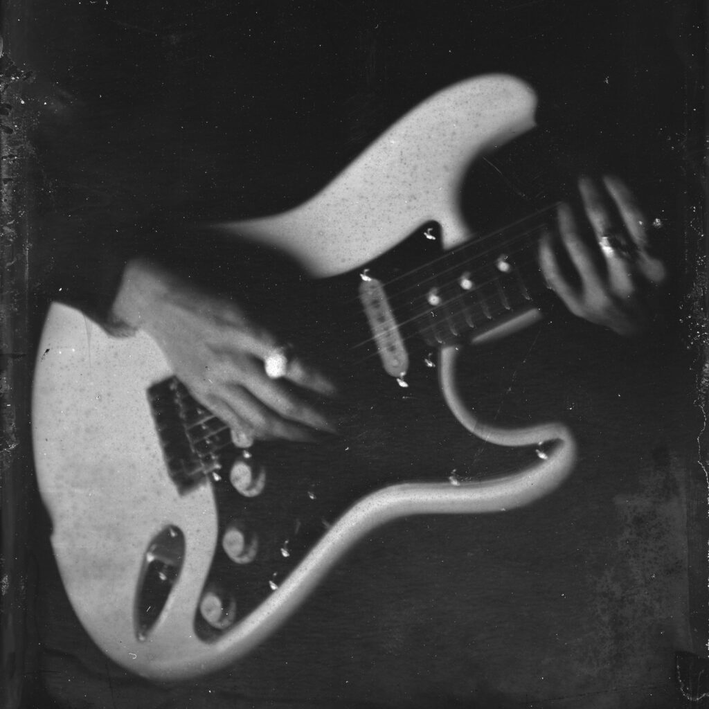 A close-up black and white image of hands playing an electric guitar