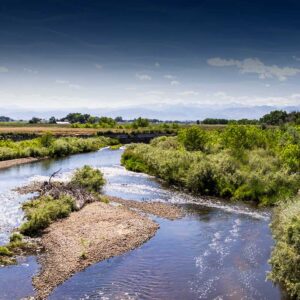 St. Vrain and Left Hand stream water with grassy embankment blue sky and mountains in the background