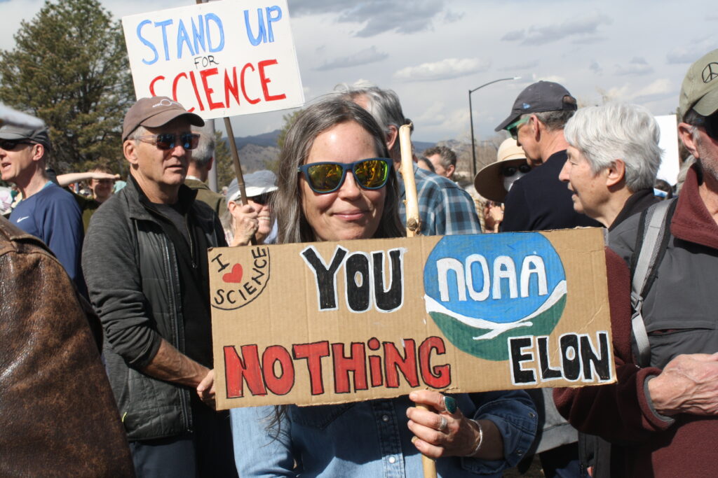 Woman holding sign at protest that says "You NOAA nothing Elon" 